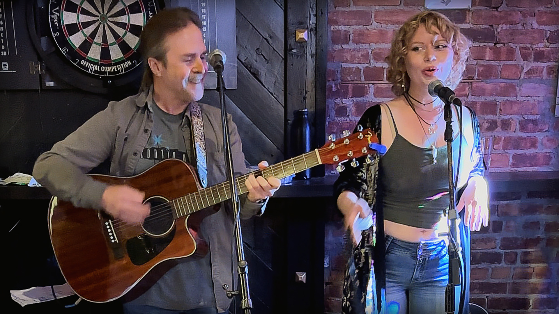 A curry haired women singing and a man playing guitar